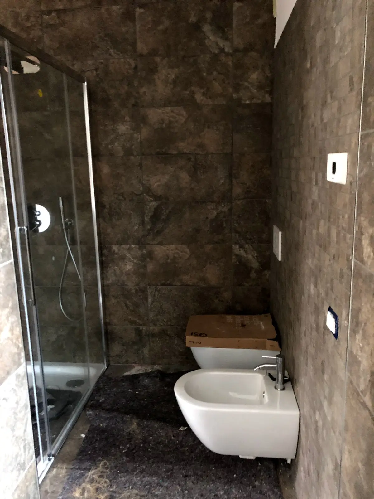 Bagno ristrutturato con rivestimenti scuri, doccia e sanitari sospesi